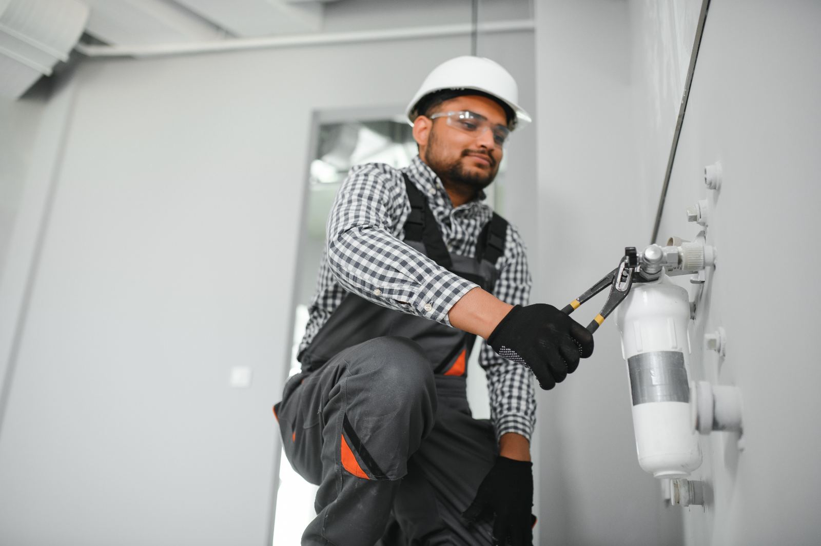 Technician installing a wall-mounted water filtration housing with pliers